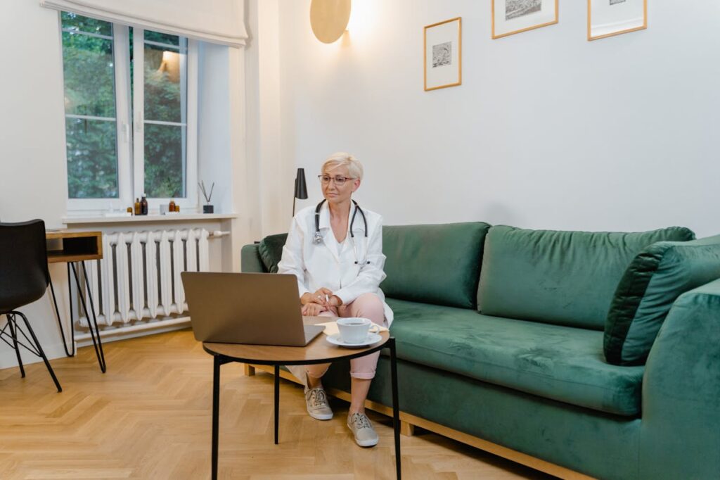 A female doctor sits in a cozy room, conducting a telemedicine appointment on her laptop.